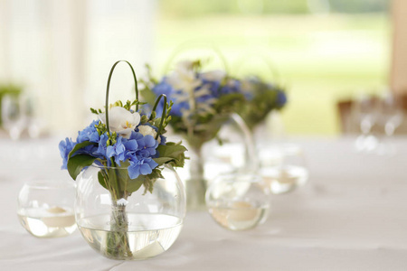 婚礼圆形玻璃花瓶中的蓝色和白色的花朵的装饰