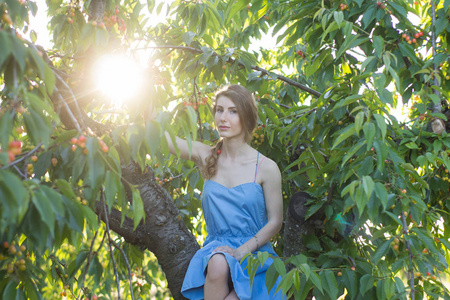 夏天时在樱桃树旁摆出蓝色连衣裙的年轻漂亮女子