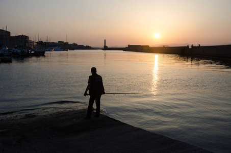 有灯塔和日落背景的渔夫的剪影。日落时分, 希腊海上日落, 干尼尼。金黄橙色日落