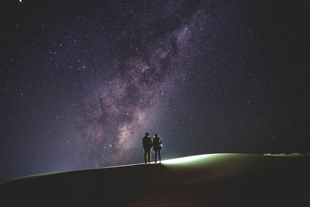 景观与银河。夜的天空与星和剪影一对站立的夫妇在沙子山