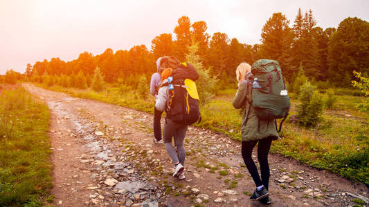 两个徒步旅行的妇女带着背包沿着小路走到山上, 在一个温暖的夏日里