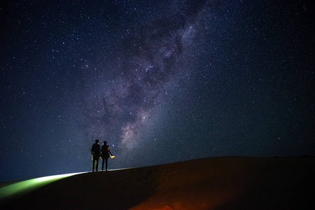 景观与银河。夜的天空与星和剪影一对站立的夫妇在沙子山