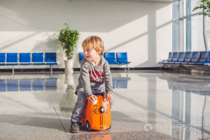 在机场的橙色手提箱的可爱小男孩