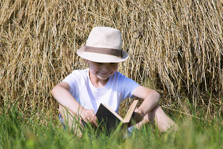 夏天, 可爱的小男孩正在草地上的稻草堆里看书。