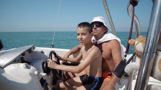 游艇船长手上游艇方向盘, 当地男子教小男孩如何驾驶游艇上的准帆肾上腺素骑行游