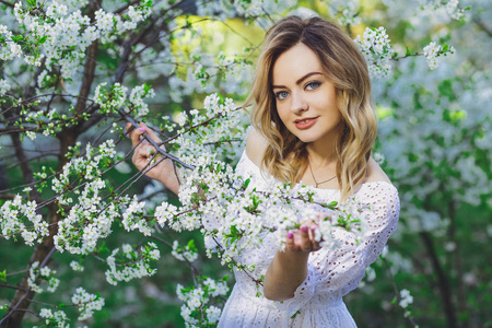 美丽的金发女孩与金发在礼服上的春天盛开的树木背景