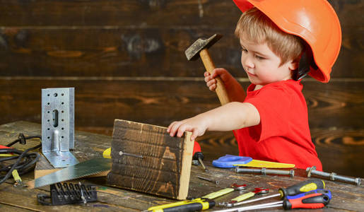 幼儿在繁忙的脸上玩锤子工具在家中的车间。小男孩扮演杂工。就要手工制作概念。儿童头盔可爱的发挥建设者或维修, 修理或就要手工制作