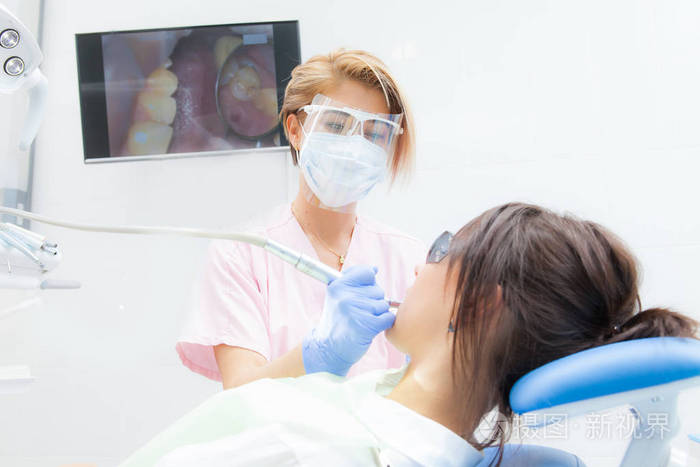 一位女牙医正在用黑发治疗女孩的牙齿。戴手套面具和护目镜的医生
