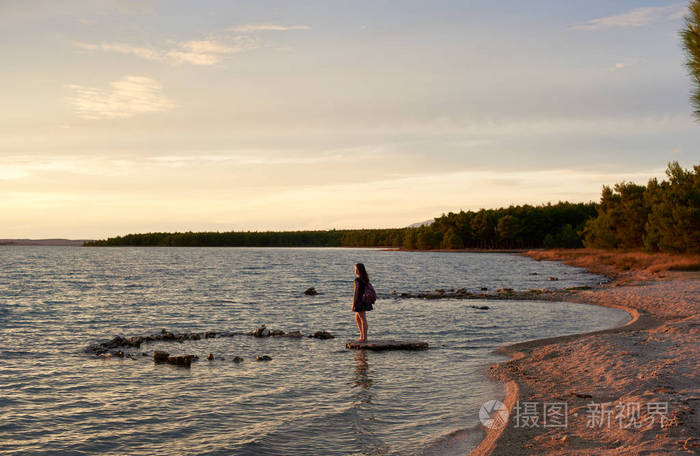 年轻女子穿着短裙, 带着五颜六色的背包, 独自一人在平坦的石头上赤脚