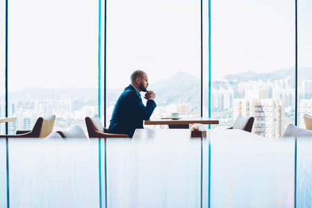体贴聪明的男性企业家穿着正式的服装思考在重要的商务会议上坐在咖啡餐厅与玻璃窗口。商业文本广告区域