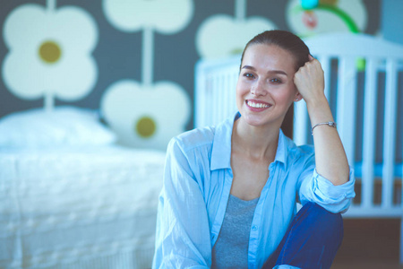 年轻的女人坐在儿童床边的地板上。年轻的妈妈