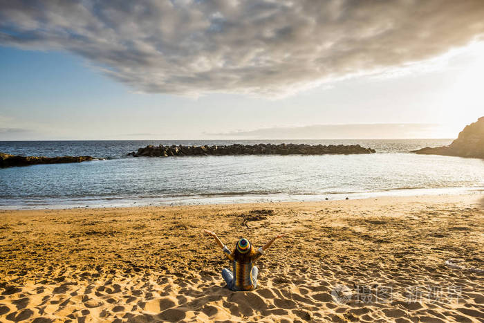 坐在海滩和拥抱海洋的年轻妇女的后方看法
