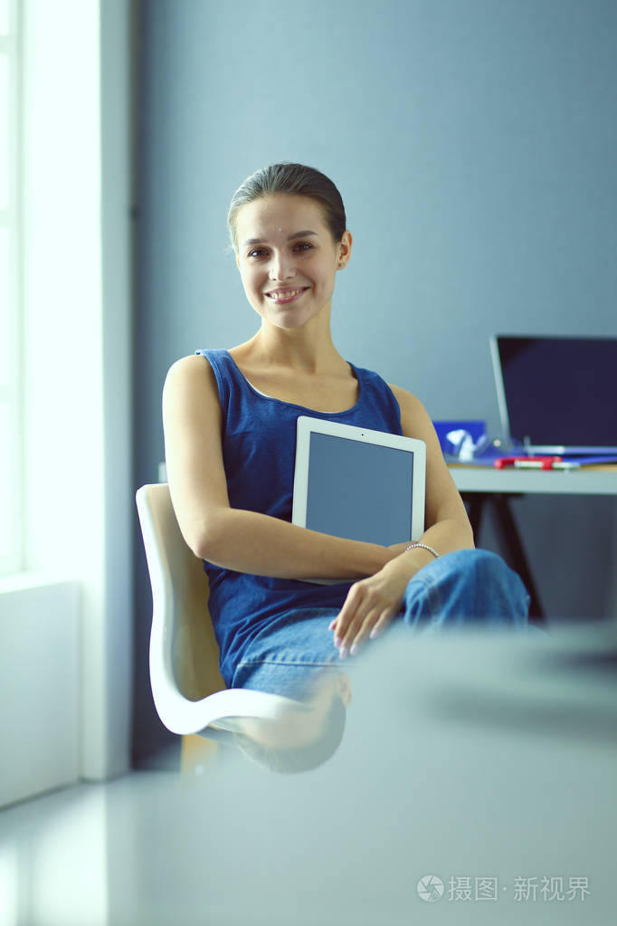 年轻的女人坐在办公桌前与文书, 计划和笔记本电脑