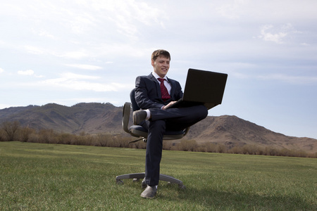 坐在椅子上的绿色草地上笔记本电脑的商人
