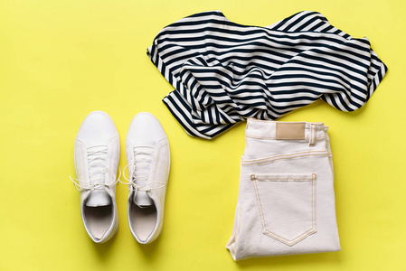 女性白色运动鞋和牛仔裤, 条纹 t恤在黄色背景与拷贝空间。顶部视图。夏季时尚, 胶囊衣柜概念。创意平躺