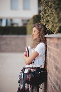 女学生站在墙上, 手里拿着书, 肩上拿着书包。