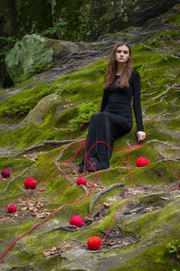 一个美丽的女孩坐在绿色的苔藓在一个童话森林。在黑色的礼服, 躺在绿色的青苔, 和周围散落的红线球的黑发肖像