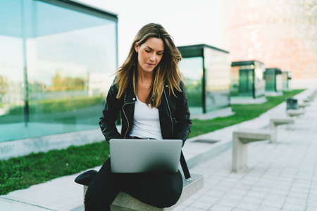 年轻记者女性工作在新的文章, 而坐在城市公园与便携式计算机连接到 wifi。时髦的女孩在时尚的衣服在线聊天由笔记本电脑户外