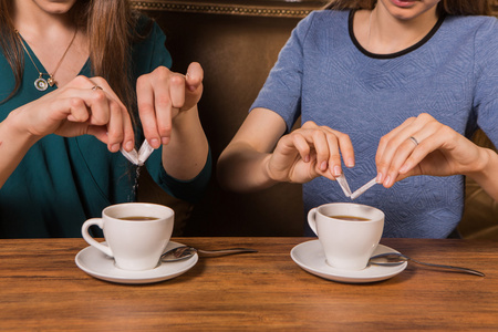 手中两个女人把糖放在一杯咖啡