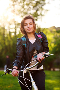 梦幻般的年轻女子在日落绿色公园上自行车