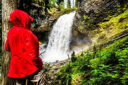 穿着红色雨衣的女人看着 Moul 瀑布的巨大水流, 位于加拿大不列颠哥伦比亚的清水溪灰色省级公园。