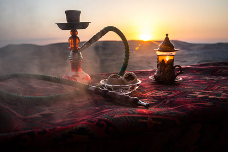 水烟碗里的水烟热煤, 在户外沙漠中制造蒸汽云。东方饰品在地毯东方茶道。时尚东方水烟日落背景。选择性聚焦