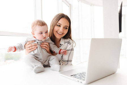 快乐的年轻女子的母亲使用笔记本电脑与她的小儿子在家中的孩子的形象
