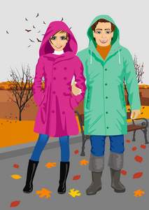 穿着雨衣站在公园在秋天里的年轻夫妇