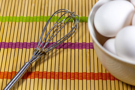 一组鸡蛋在一个深白色的碗旁边的一个搅拌等待厨师使用他们在一餐竹垫