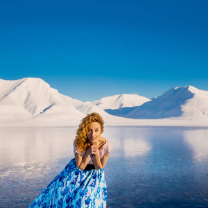 女孩纤细漂亮的红头发的背景在斯匹次卑尔根市朗伊尔城山斯瓦尔巴特群岛上结了霜的蓝色礼服