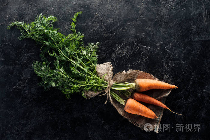 黑色大理石表面上用绳子拴在麻布上的新鲜熟胡萝卜的顶部视图