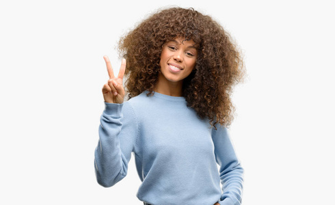 非洲裔美国妇女身穿毛衣显示和指向两个手指, 而微笑着自信和快乐
