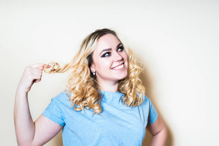 在明亮的背景上的金发女人变成手指缕头发照片