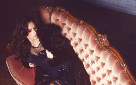美丽的女人坐在沙发上的黑色礼服