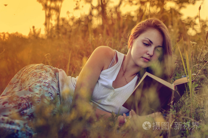 读一本书在一片草地上的漂亮女孩