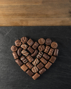 美丽的创意巧克力心形制成的各种类型的果仁糖在一个黑色的石头背景。甜蜜的巧克力在黑暗的背景下