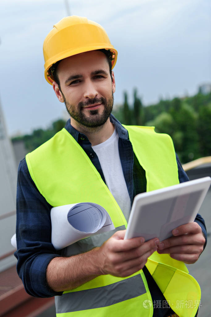 男工程师在安全背心和头盔 holsing 蓝图和数码片