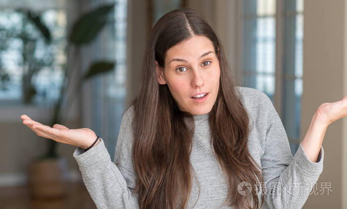 年轻漂亮的女人在家里无能和困惑的表达与手臂和双手提出.怀疑概念