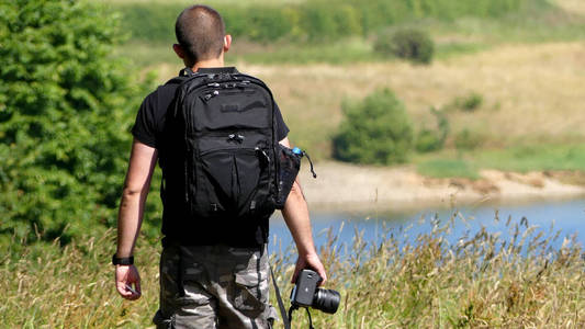 一名男摄影师向湖边走去, 穿着短裤和背包, 相机在他身边.照片