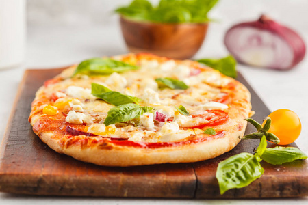 椭圆形自制比萨与羊乳酪, 西红柿和洋葱在木板上