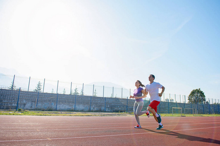 年轻的运动情侣在阳光明媚的日子在体育场跑道上慢跑