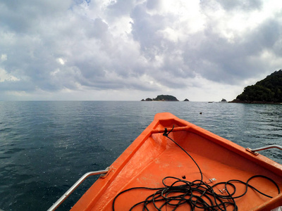 纤维小船的鼻子航行到海岛. 多云的天空背景和飞溅的水