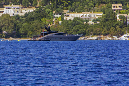 豪华现代游艇停泊在蓝海湾的科孚岛, 希腊与绿色的树木和别墅背景