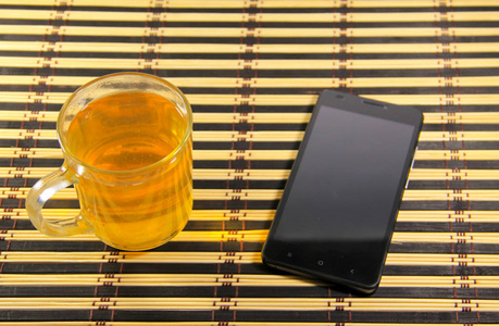 黑色的智能手机和杯茶竹垫上