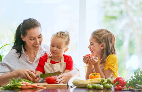 健康的食物在家里。幸福的家庭在厨房里。母亲和孩子的女儿们正在准备蔬菜。
