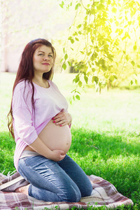 快乐怀孕女孩坐在草拥抱腹部图片