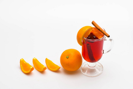 饮料或饮料与橙和肉桂。鸡尾酒和酒吧的概念。葡萄酒或热苹果酒在橙色水果附近的玻璃和白色背景切片。橙片附近的葡萄酒