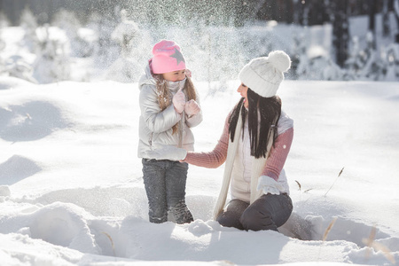 年轻漂亮的母亲和她的小女孩在户外在冬天的乐趣。开朗的孩子和她美丽的妈妈玩雪的性质