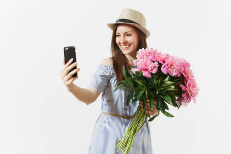 年轻女子穿着蓝色连衣裙, 帽子捧着美丽的粉红色牡丹花, 在手机上做自拍的白色背景。圣情人节, 国际妇女节节日概念