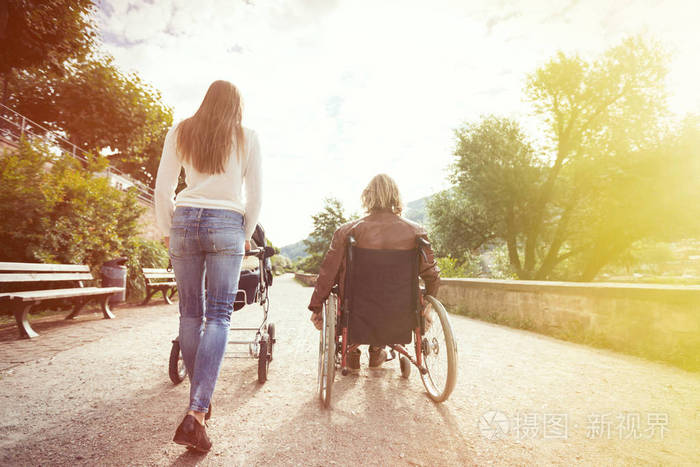 婴儿推车在公园里坐轮椅的年轻父母